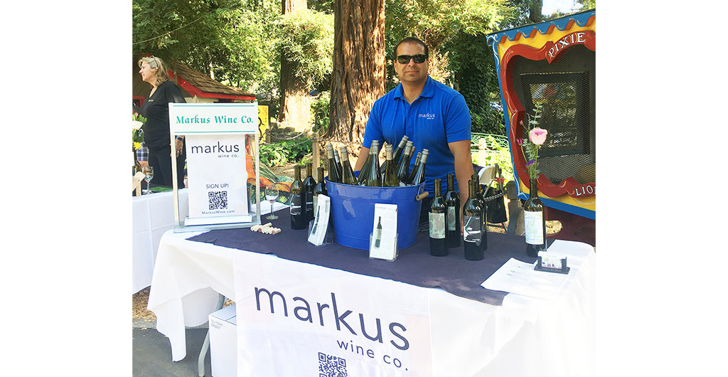 Cellarmaster Mike standing behind a table full of wine bottles with the Markus logo on the tablecloth front.