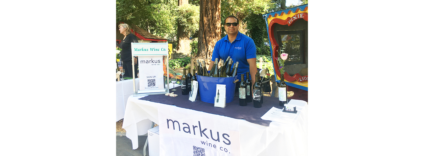 Cellarmaster Mike standing behind a table full of wine bottles with the Markus logo on the tablecloth front.
