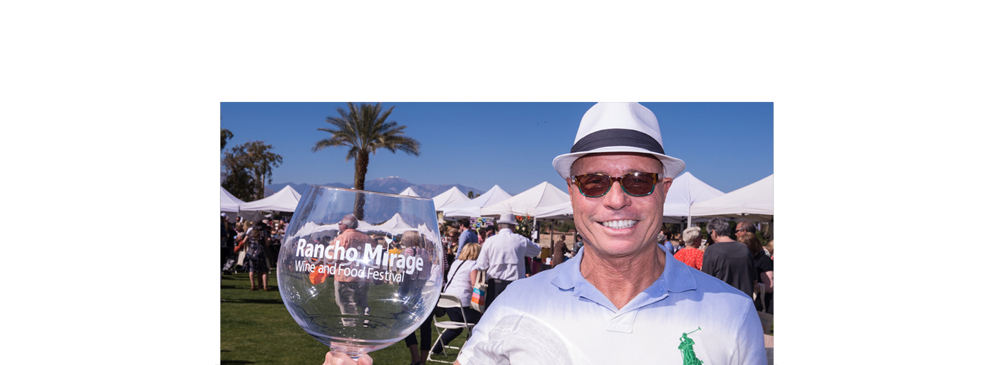 Very happy smiling man holding glass of red wine with Rancho Mirage logo.